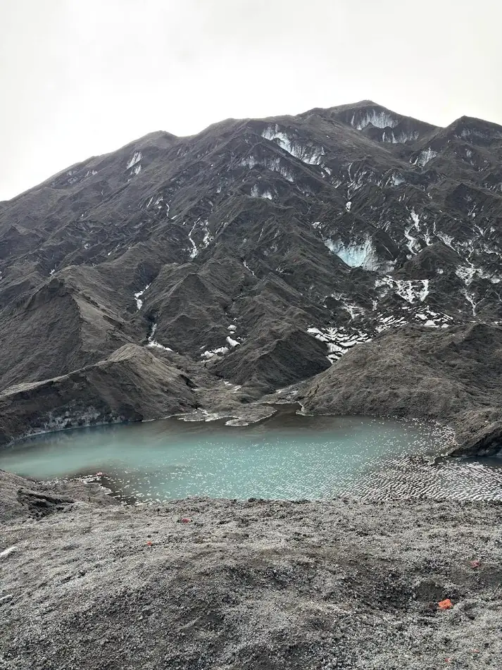 Laguna turquesa al pie de un cerro de roca oscura con restos de hielo del Glaciar Pichillancahue